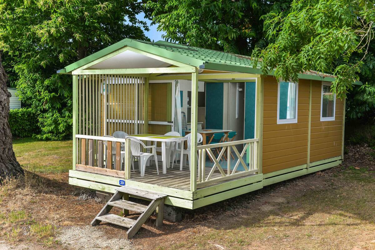 Een kleine, gelijkvloerse stacaravan met een veranda, een tafel en stoelen.