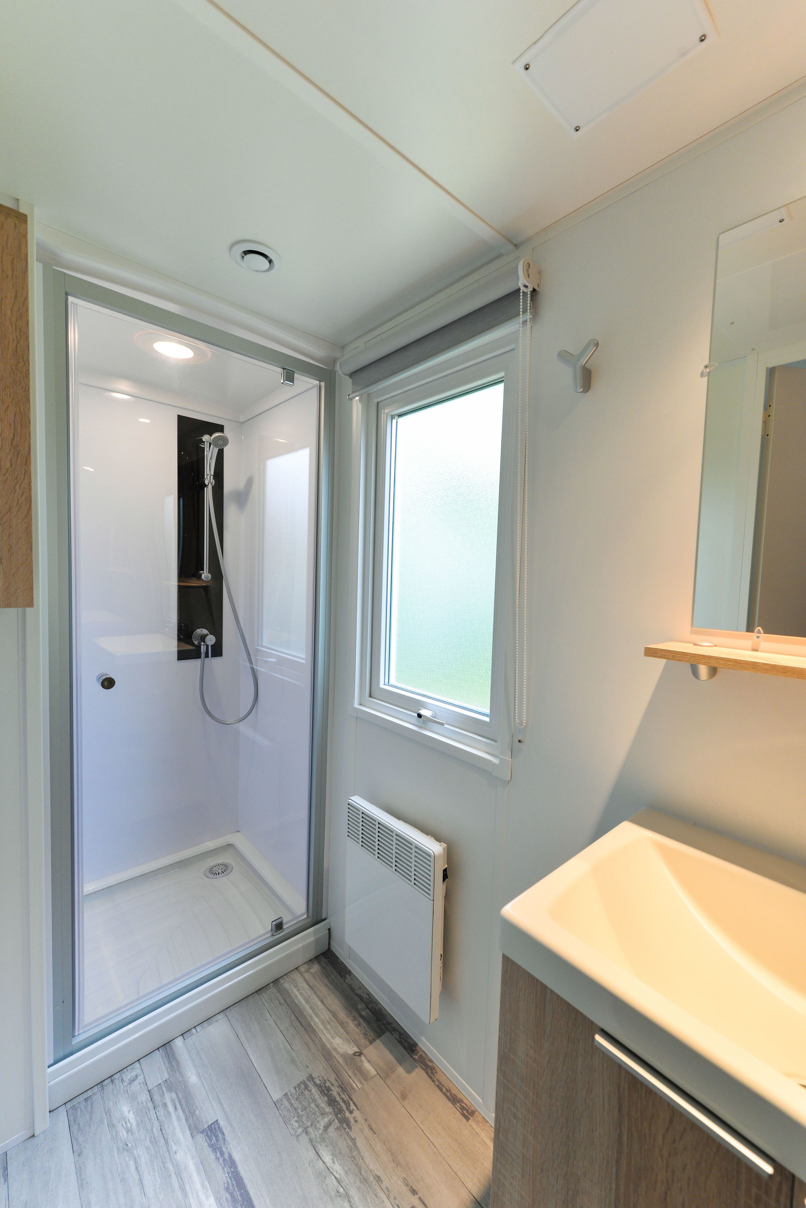 A modern bathroom with a glass-enclosed shower, a window, and a sink with a mirror.
