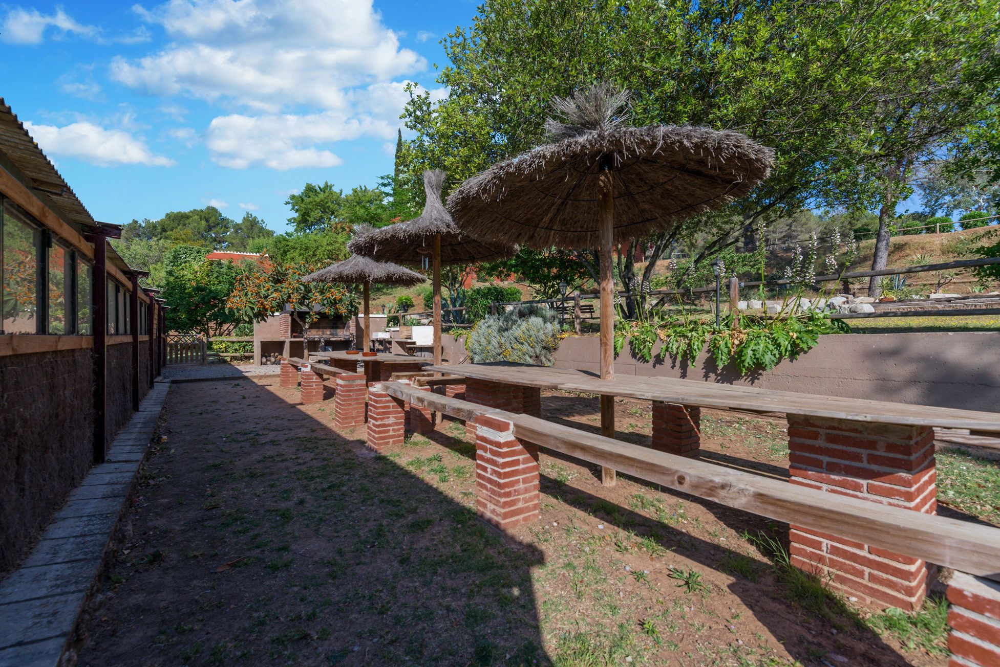 An outdoor patio with brick pillars, wooden benches, and thatched umbrellas.