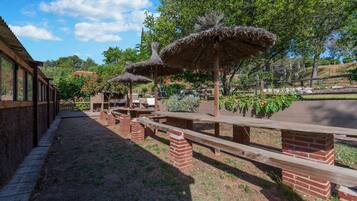 An outdoor patio with brick pillars, wooden benches, and thatched umbrellas.