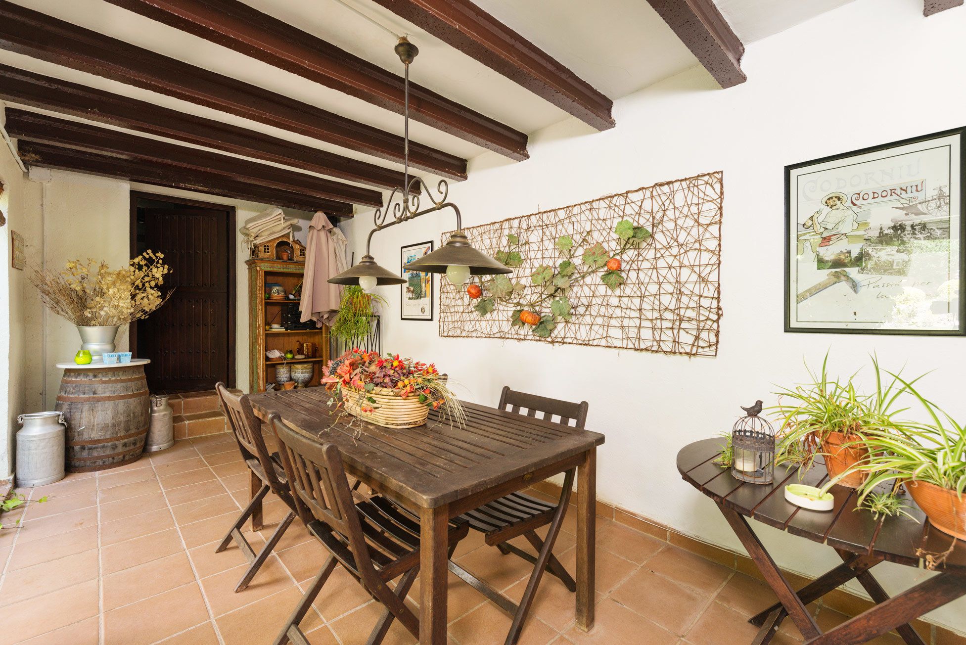 A rustic dining area with a wooden table and chairs, a hanging light fixture, and a decorative wall piece.