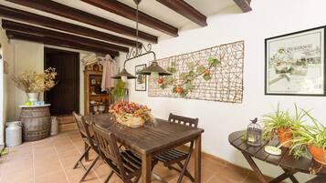 A rustic dining area with a wooden table and chairs, a hanging light fixture, and a decorative wall piece.