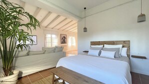 Un dormitorio con una cama, un banco, una planta en maceta y vistas a otra habitación.
