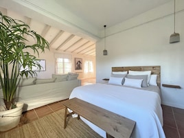 Un dormitorio con una cama, un banco, una planta en maceta y vistas a otra habitación.