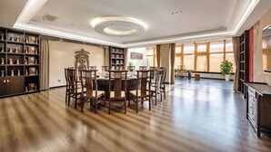 A spacious dining area with a round table and chairs, surrounded by bookshelves and a large window. - Broma Hotel (Tongchuan)
