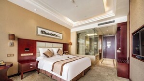 A hotel room with a large bed, a desk, a TV, and a glass-enclosed shower area. - Broma Hotel (Tongchuan)