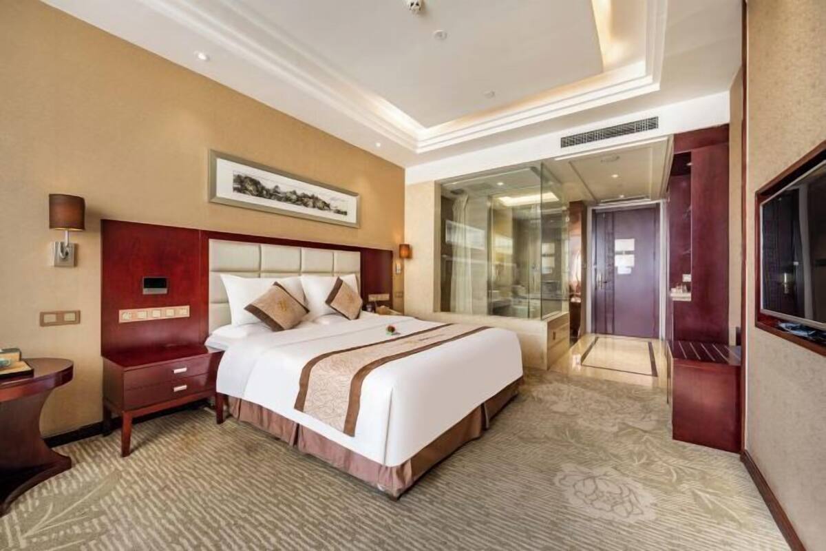 Une chambre d’hôtel avec un grand lit, un bureau, une télévision et une douche séparée par une paroi en verre.
