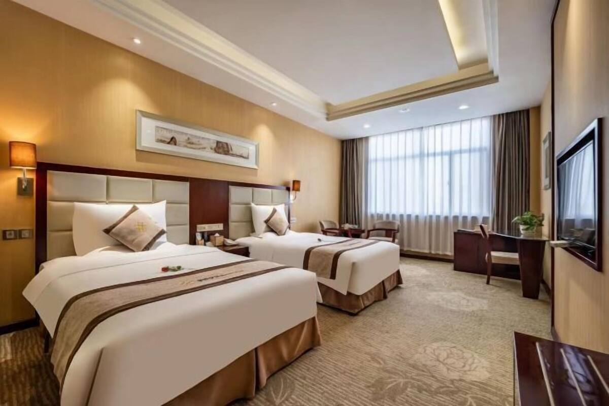 Une chambre d’hôtel avec deux lits, un bureau, une chaise et une grande fenêtre avec des rideaux.