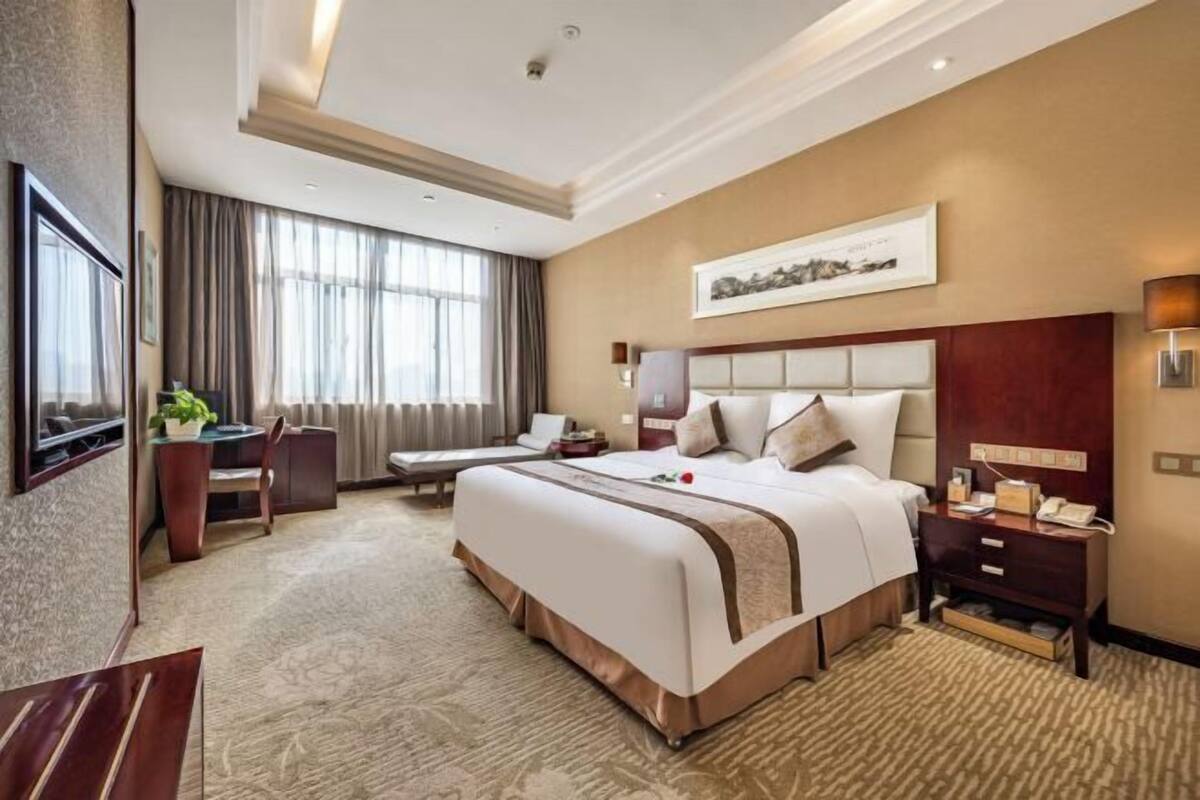 Une chambre d’hôtel avec un grand lit, un bureau, une chaise, une télévision et une fenêtre avec des rideaux.