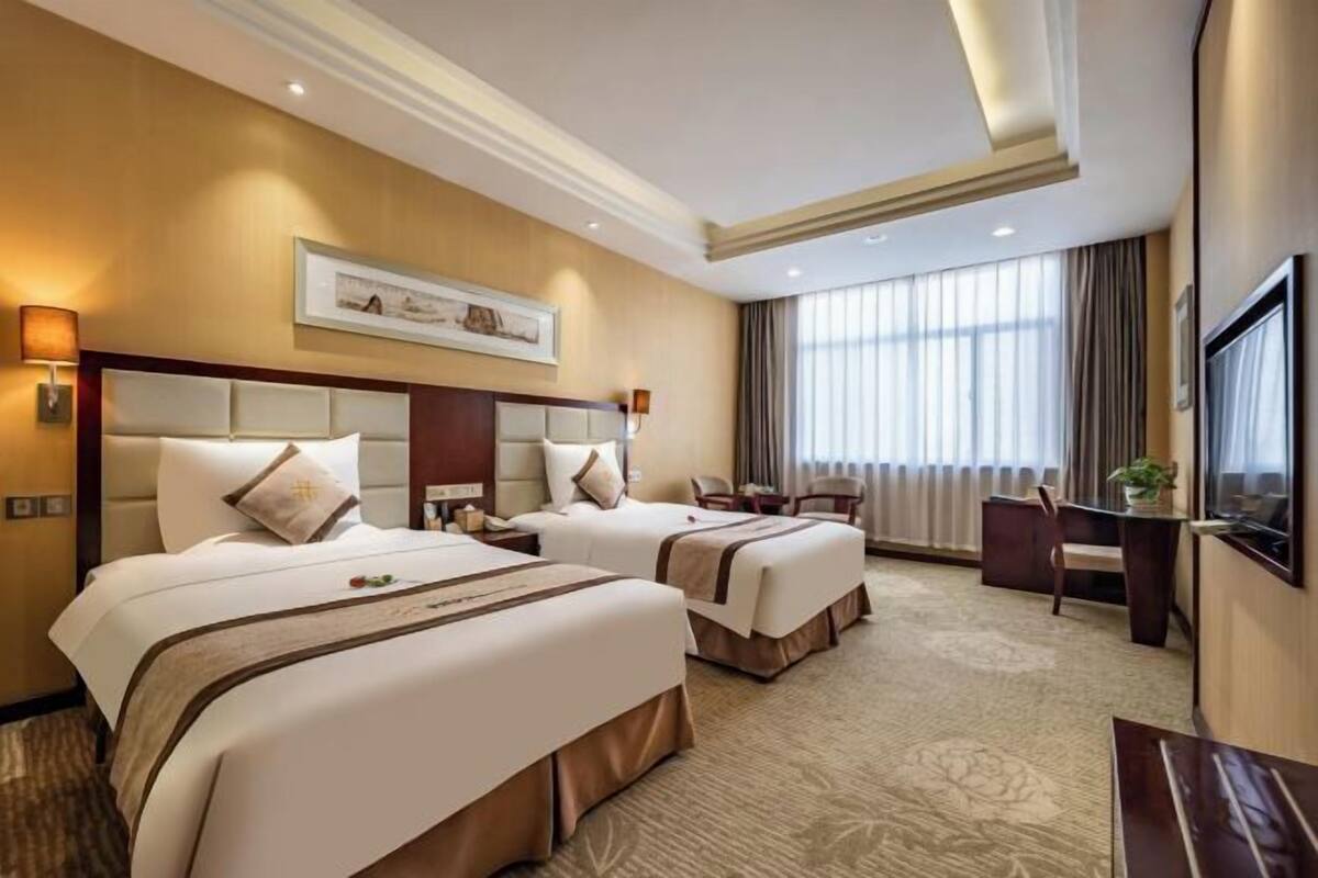 Une chambre d’hôtel avec deux lits, un bureau, une chaise, une télévision et une grande fenêtre avec des rideaux.