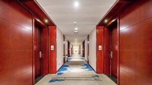 A long, narrow hallway with wooden doors on both sides and a blue carpet with arrows. - Broma Hotel (Tongchuan)