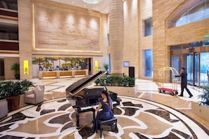 A grand lobby with a grand piano, a reception desk, and a large wall mural.