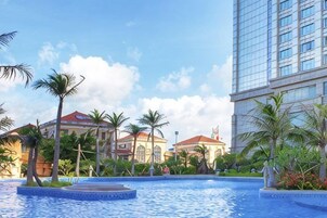 Una piscina con una fuente, rodeada de palmeras y edificios con tejados rojos.
