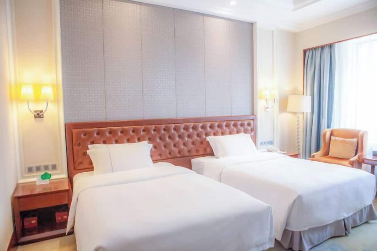 Quarto de hotel com duas camas, uma cabeceira grande e acolchoada, e vista da cidade pela janela.