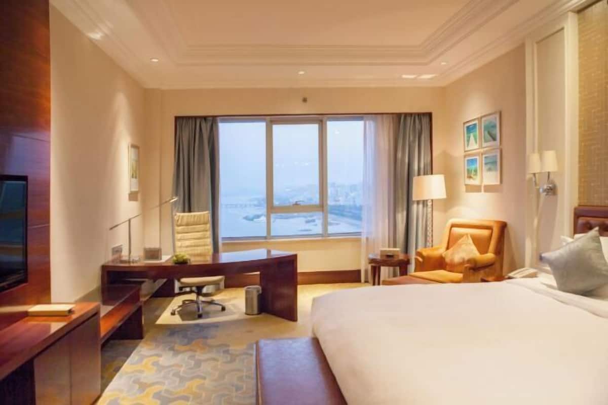 Quarto de hotel com uma cama grande, uma escrivaninha, uma cadeira, uma televisão e vista para a cidade.