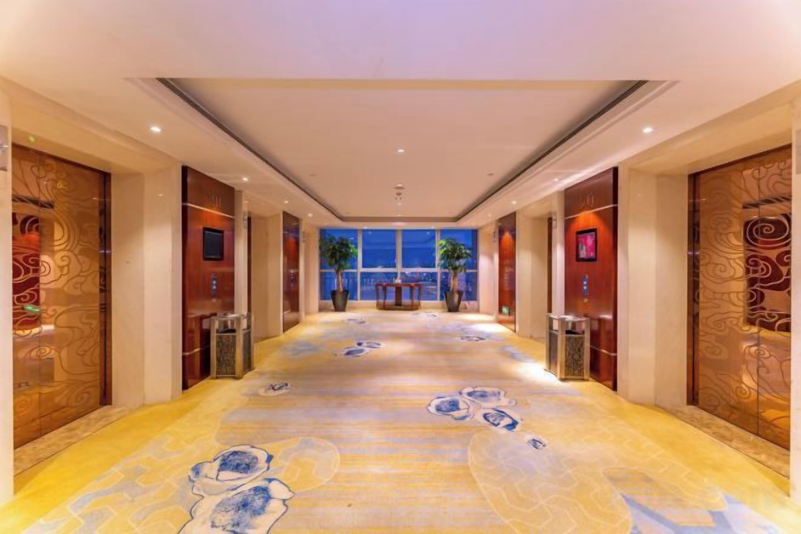 A hotel corridor with patterned flooring, wooden doors, and a view of the city at night.