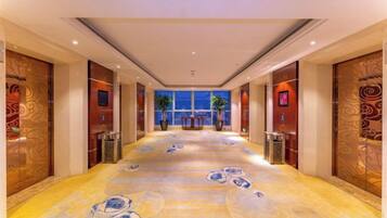 A hotel corridor with patterned flooring, wooden doors, and a view of the city at night.