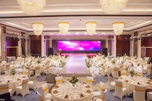 Un salón de banquetes con mesas redondas, candelabros y un escenario con un telón de fondo morado.