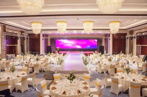 Un salón de banquetes con mesas redondas, candelabros y un escenario con un telón de fondo morado.