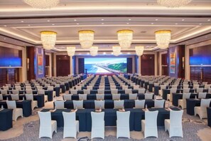 Une salle de conférence avec des rangées de chaises, un grand écran à l’avant et des lustres.