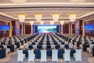 Un salón de conferencias con filas de sillas, una pantalla grande al frente y candelabros.