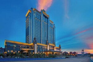 Un hotel moderno de gran altura, con un diseño arquitectónico destacado, una entrada imponente y un amplio estacionamiento al frente.