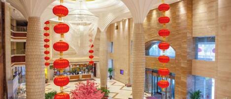 A spacious lobby with a central decorative tree, multiple red lanterns, and a chandelier.