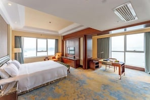 A hotel room with a large bed, a desk, a television, and a view of the sea. - Glory Charm Hotel (Fangchenggang)