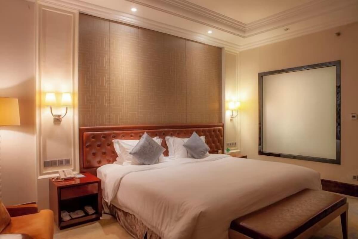 A hotel room with a large bed, two bedside tables, a nightstand, a bench, and a large mirror.