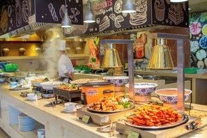 A buffet with various food items and a chef in the background.