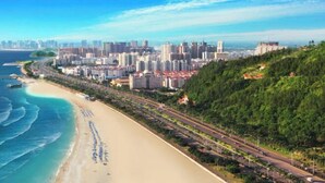 Eine Küstenstadt mit Strand, Hochhäusern und einer Autobahn.
