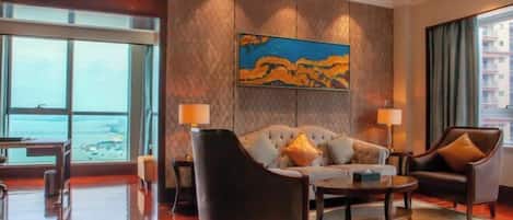 A hotel room with a large window, a sofa, a chair, a coffee table, and a painting on the wall.