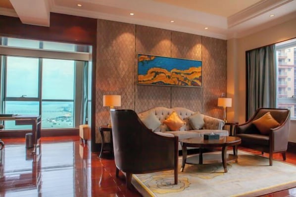 A hotel room with a large window, a sofa, a chair, a coffee table, and a painting on the wall. - Glory Charm Hotel (Fangchenggang)
