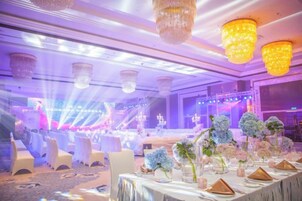 A banquet hall with tables set for a formal event, chandeliers, and a stage with lighting.