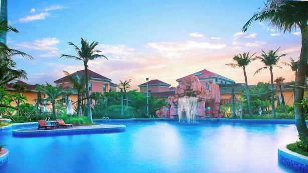 Ein Resort-Pool mit Palmen, einem Wasserfall und einem Gebäude mit rotem Dach.