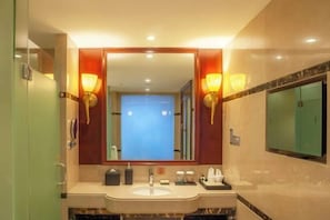 A hotel bathroom with a large mirror, two wall-mounted lights, a sink, and a vanity. - Glory Charm Hotel (Fangchenggang)