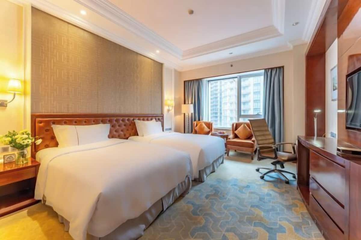 Quarto de hotel com uma cama grande, uma escrivaninha, uma cadeira, uma televisão e uma janela com cortinas.