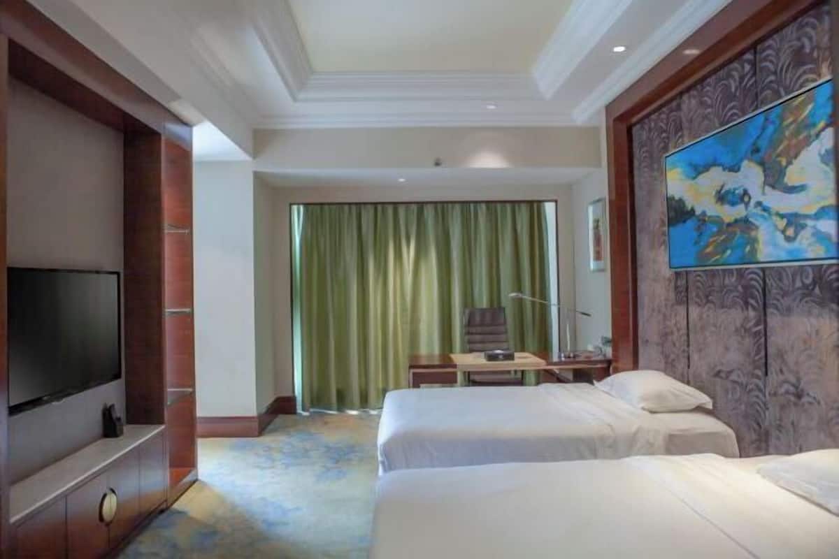 Quarto de hotel com duas camas, televisão, escrivaninha com cadeira e um quadro na parede.