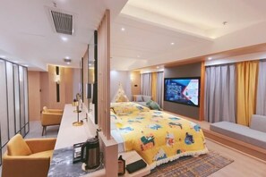 A hotel room with a bed, a TV, a desk with a kettle, and a sofa.