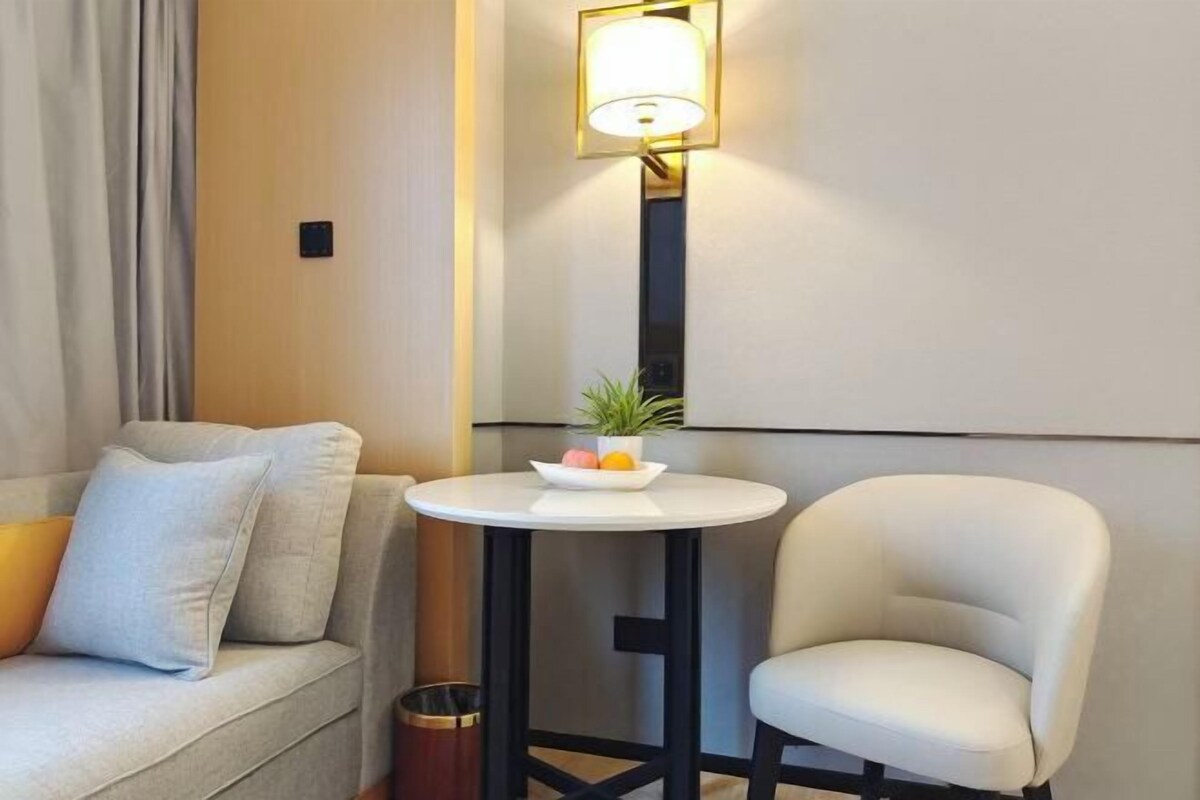 A modern room with a sofa, a chair, a small round table with a plant, and a wall-mounted lamp.