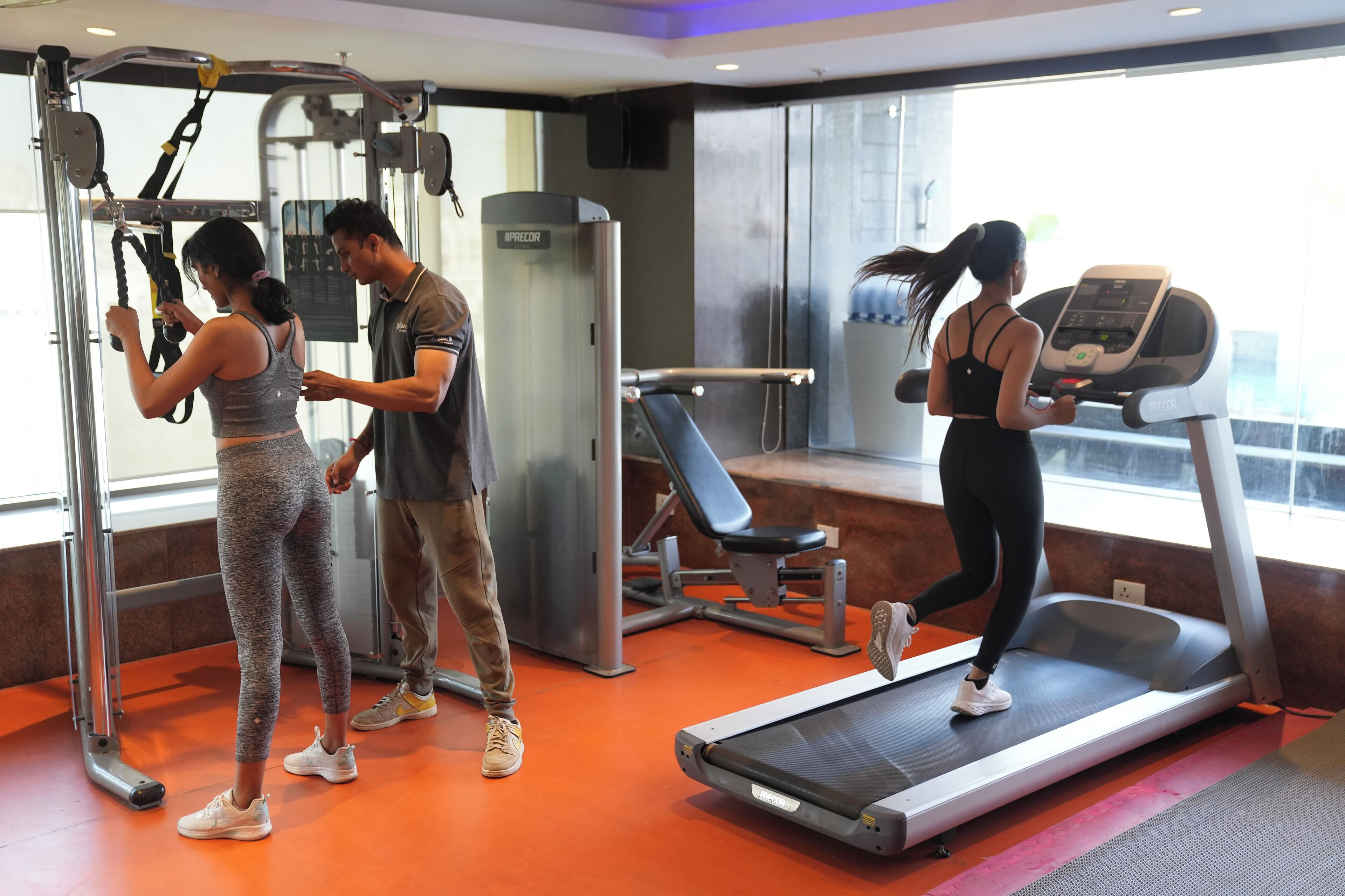 Ein Fitnessraum mit Trainingsgeräten, Laufband und großen Fenstern.
