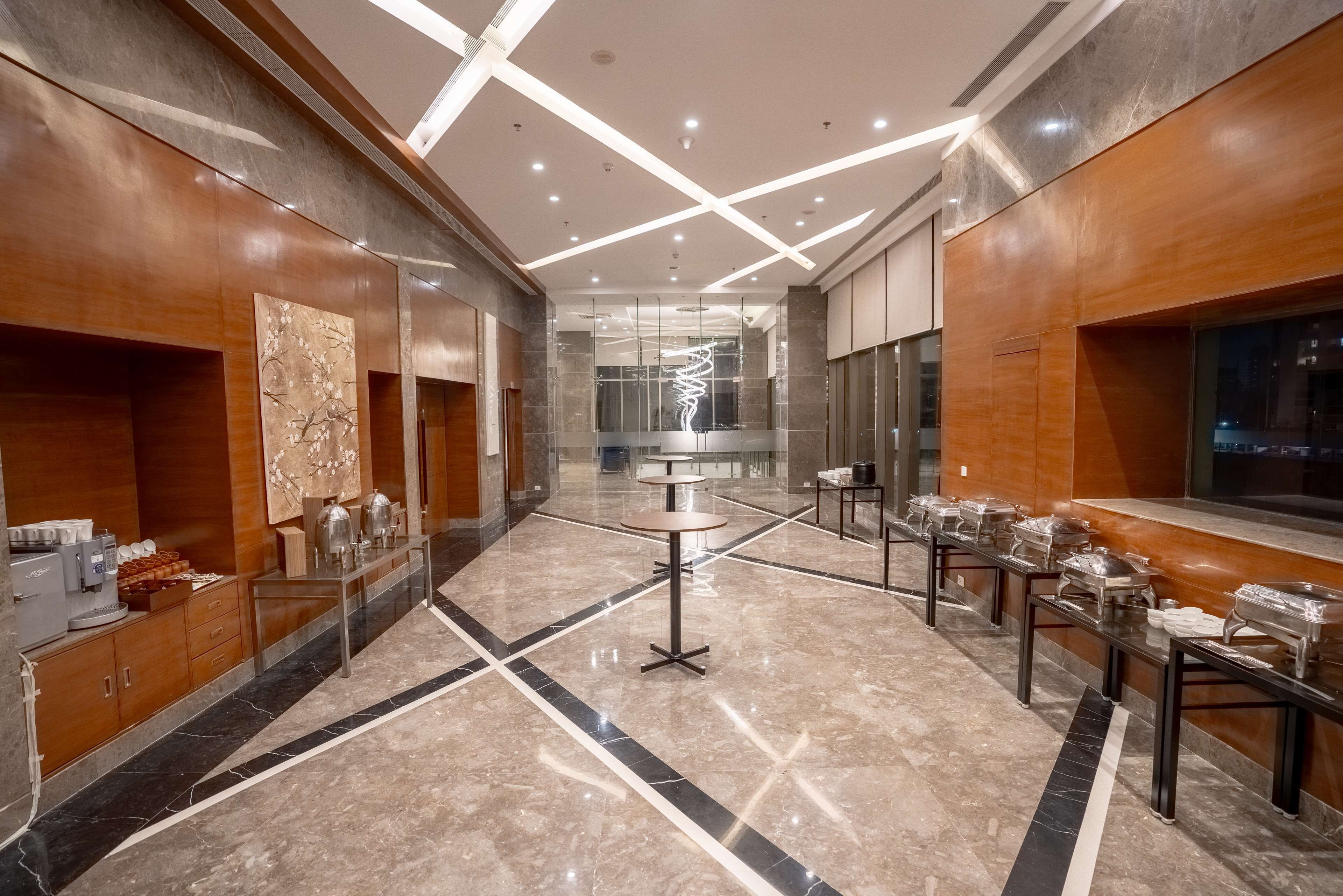 A modern hotel lobby with a marble floor, wooden paneling, and a central round table with a glass top.