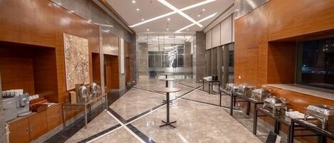 A modern hotel lobby with a marble floor, wooden paneling, and a central round table with a glass top.
