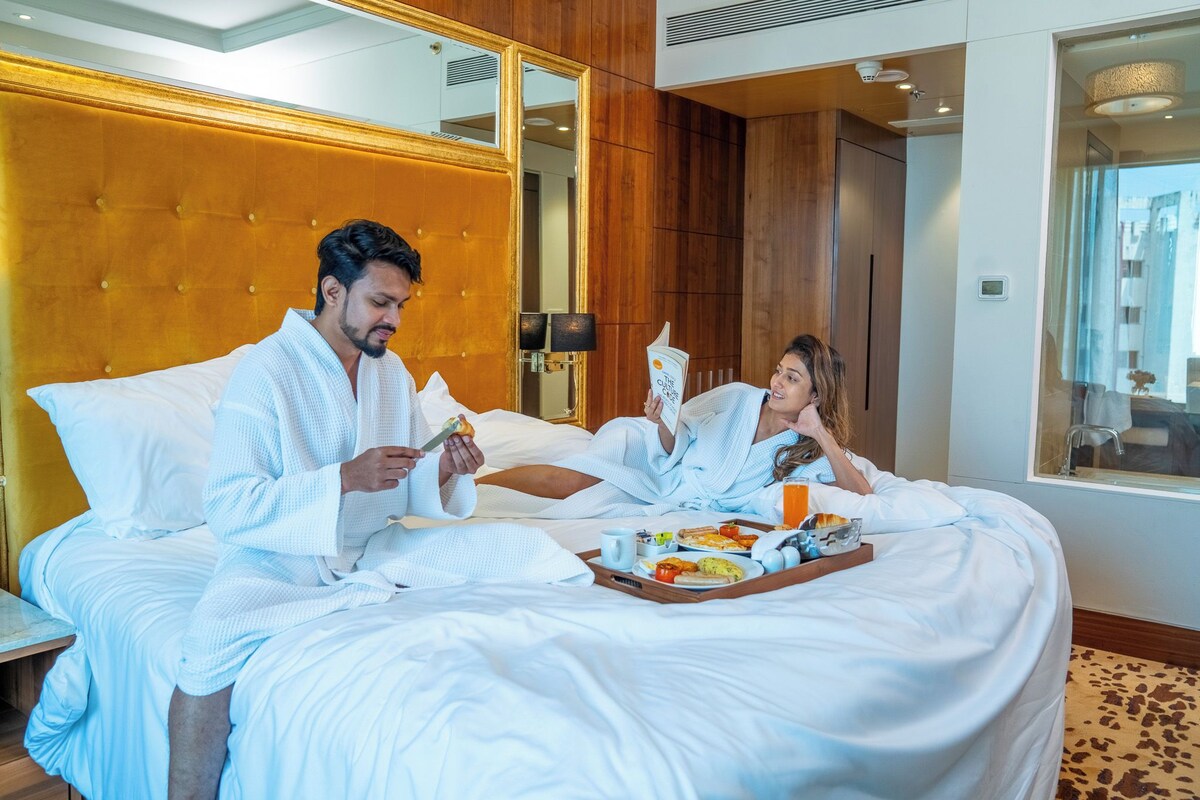 A hotel room with a large bed, a tray of breakfast, and a mirror.