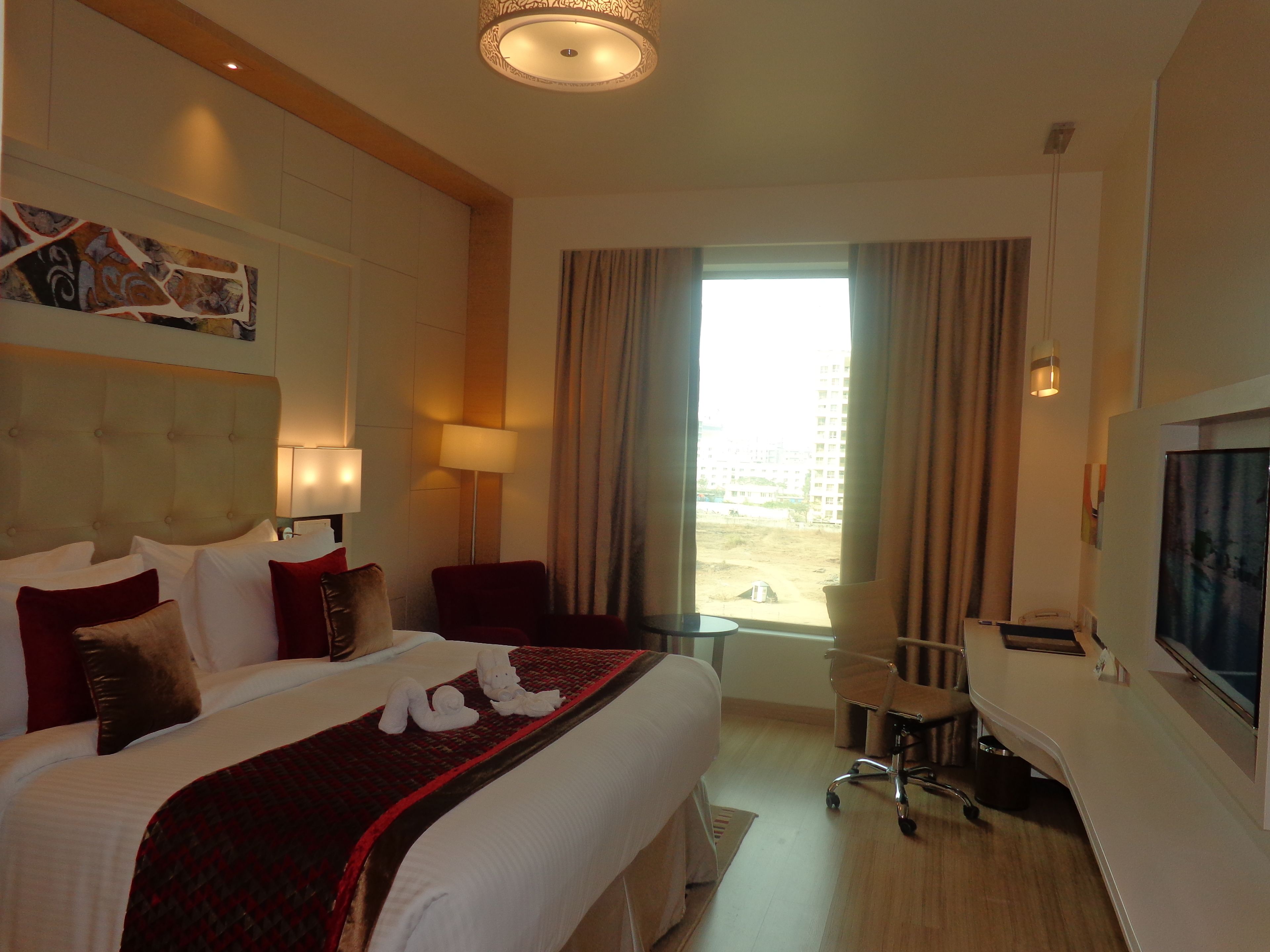 Habitación de hotel con una cama grande, un escritorio, una silla, un televisor y una ventana con cortinas.