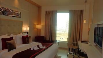 Habitación de hotel con una cama grande, un escritorio, una silla, un televisor y una ventana con cortinas.