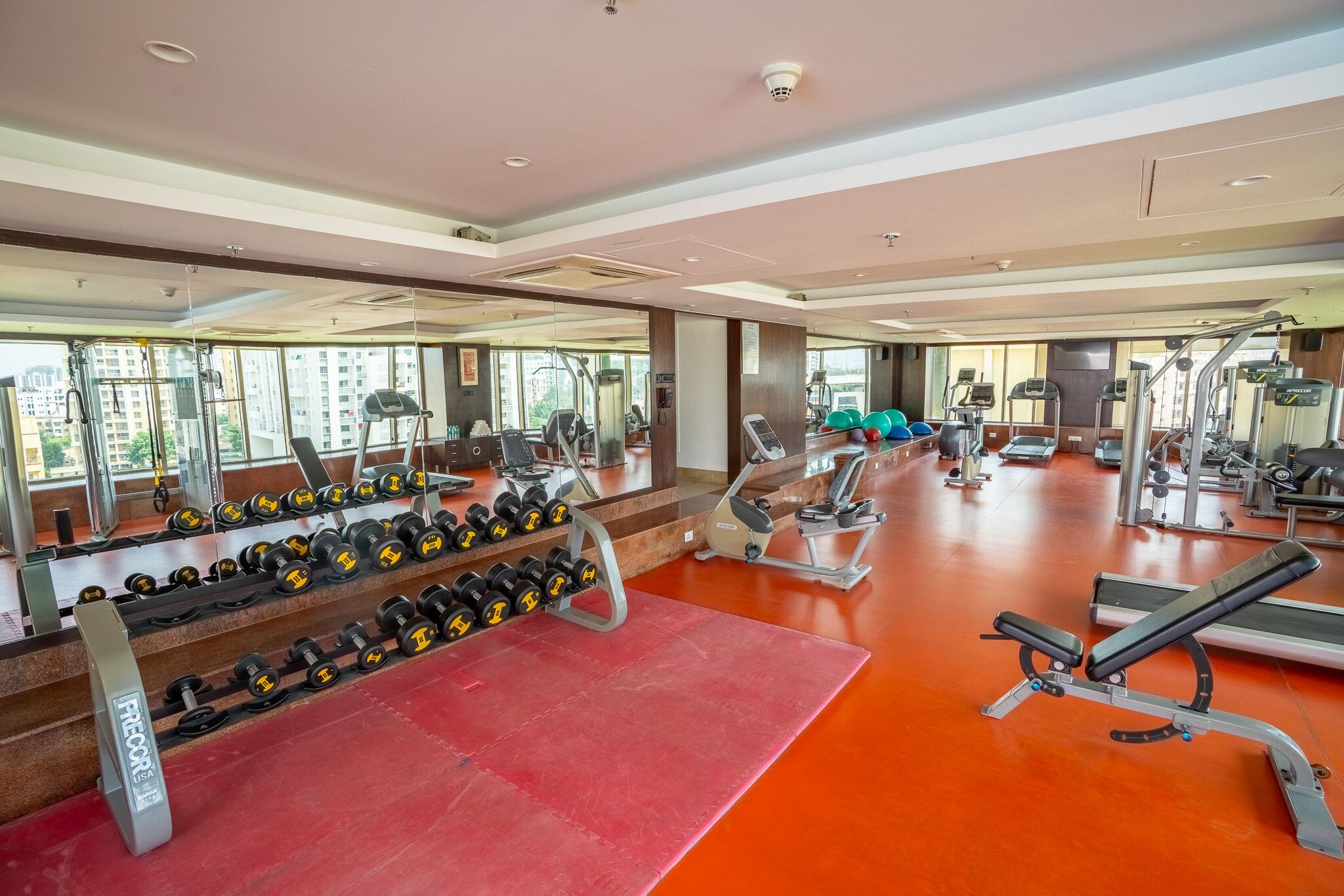 Un gimnasio con equipo de ejercicio, espejos y suelo rojo.