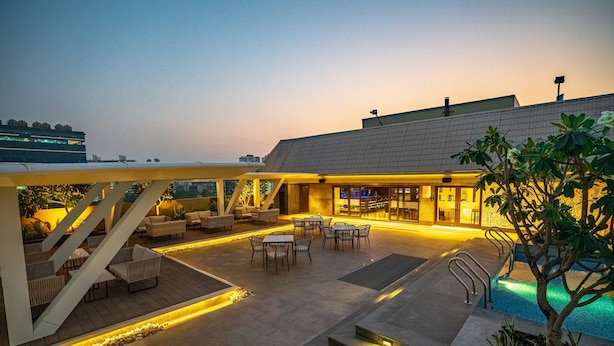A rooftop patio with outdoor seating, a swimming pool, and a building with illuminated windows. - Radisson Blu Pune Hinjawadi (Paud)
