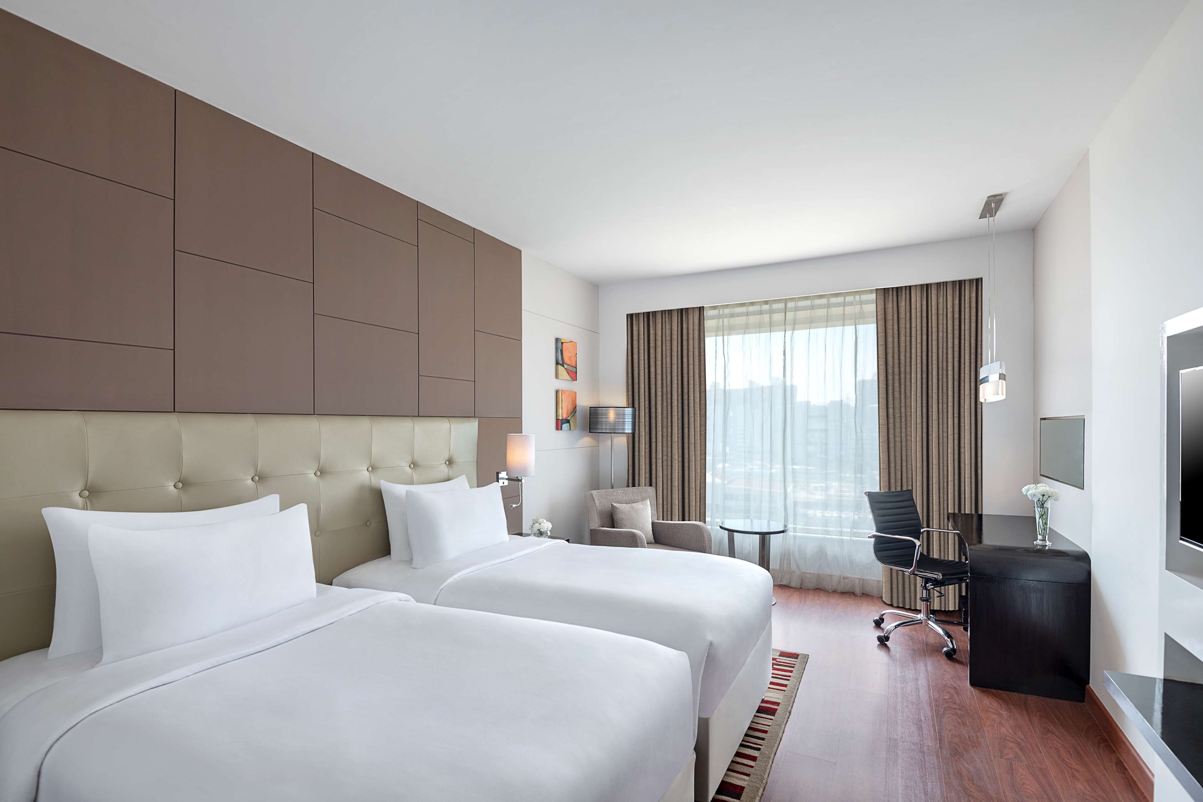 A hotel room with two beds, a desk, a chair, and a TV.