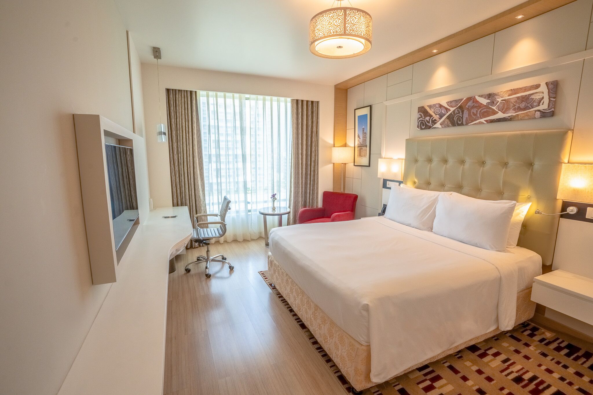 Une chambre d’hôtel avec un grand lit, un bureau, une chaise, une télévision et une fenêtre avec des rideaux.